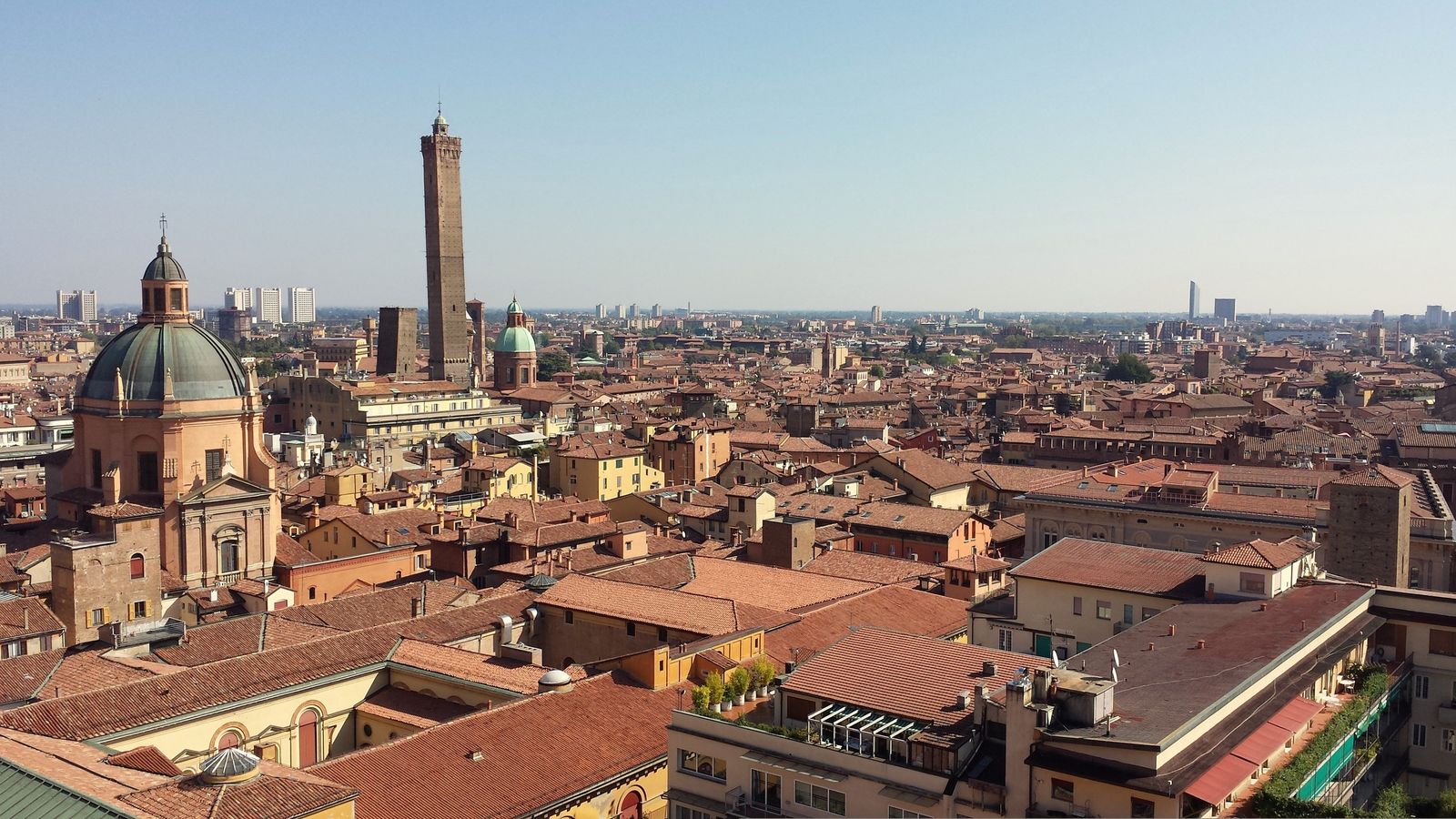 Bologna’s terracotta rooftops seen from above, with the Asinelli and Garisenda towers and church domes.